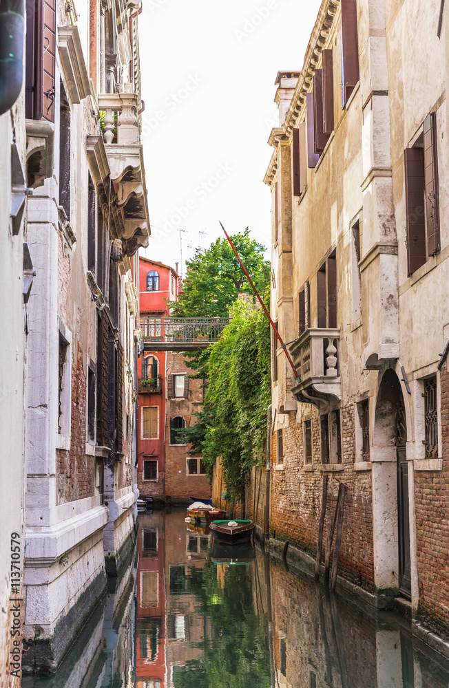  Narrow canal among old colorful brick houses in Venice, Italy.