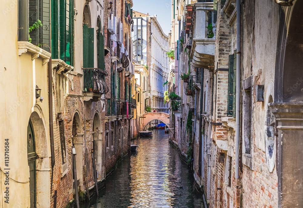  Narrow canal among old colorful brick houses in Venice, Italy.