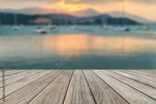 Wood table top with blurred sunset on the beach and sailing boat background