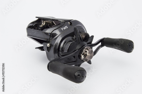 Black fishing baitcasting reel or multiplying reel. Isolated side view from the pens on uniform white background. One of the essential elements of fishing equipment