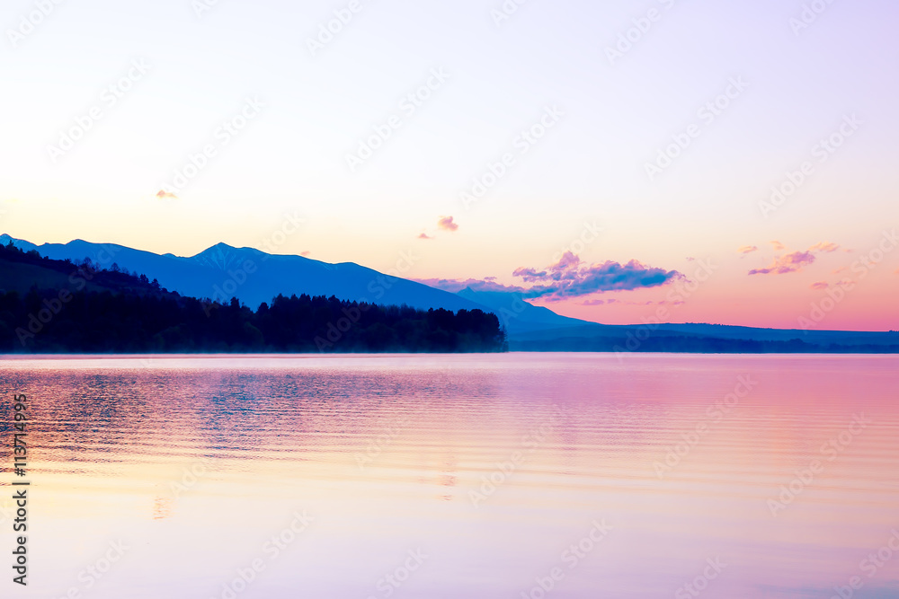 beautiful landscape with mountains and lake at dawn in golden, blue and purple tones.