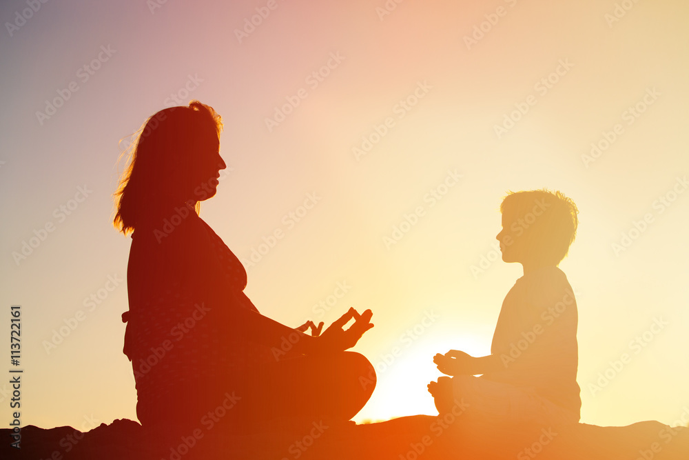 Silhouette of mother and son doing yoga on beach