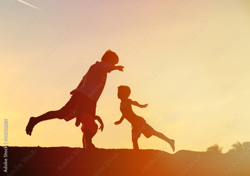 father with kids silhouettes having fun at sunset