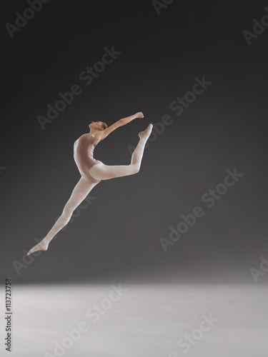 Beautiful ballerina posing in jump on gray background