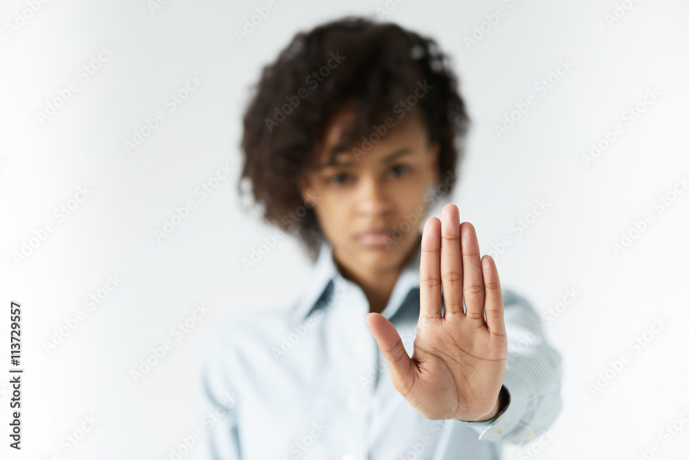 Selective focus on a palm of African teenage girl with long thin fingers, looking at the camera with serious face, extending arm, gesturing stop sign with her hand, expressing rejection or warning Selective focus on a palm of African teenage girl with long thin fingers, looking at the camera with serious face, extending arm, gesturing stop sign with her hand, expressing rejection or warning