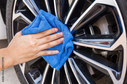 Hand with blue microfiber cloth cleaning car wheel. photo