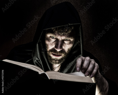 necromancer casts spells from thick ancient book by candlelight on a dark background