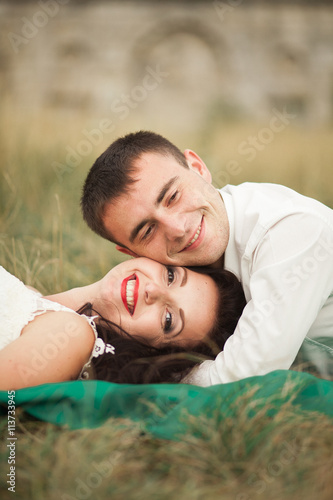 Happy wedding couple lying on green grass at the summer time