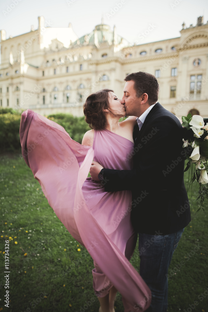 Naklejka premium Wedding. Couple. Krakow. The bride in a pink dress and groom posing on background of theater