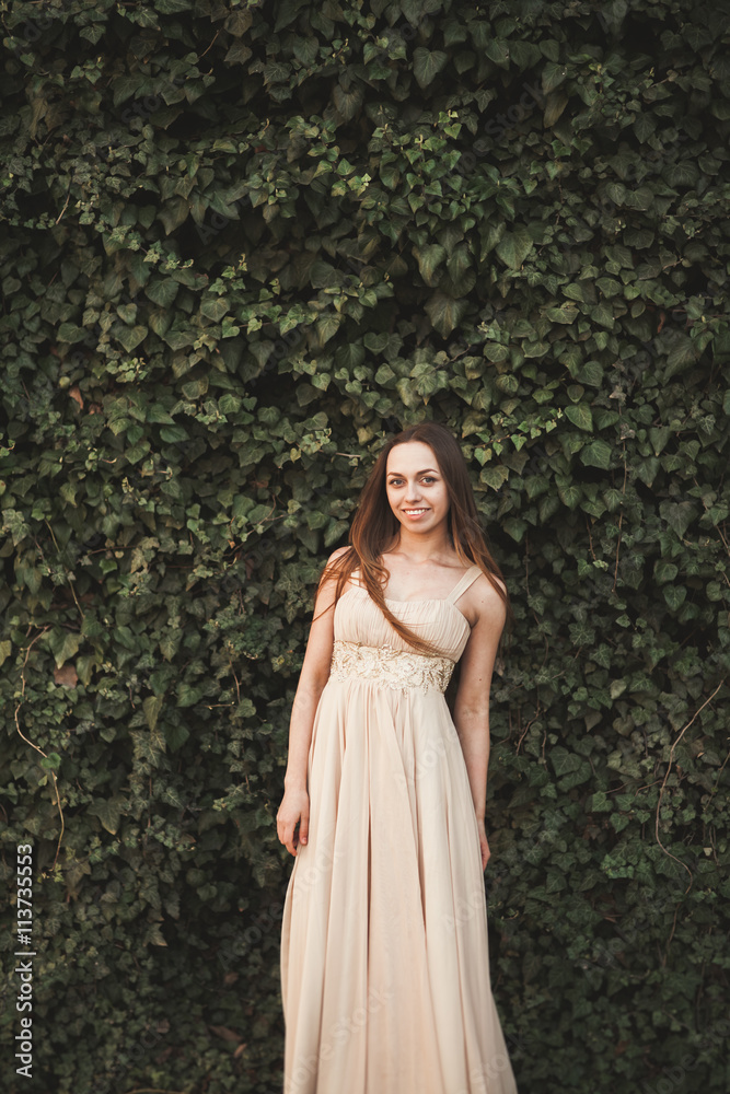 Beautiful girl, model near the wall of leaves and bushes in park
