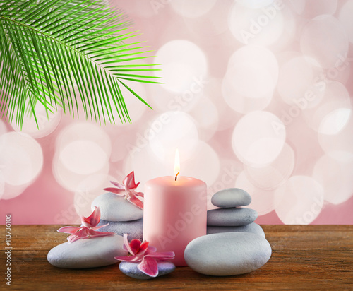 Spa stones with burning candle and flowers on pink festive background