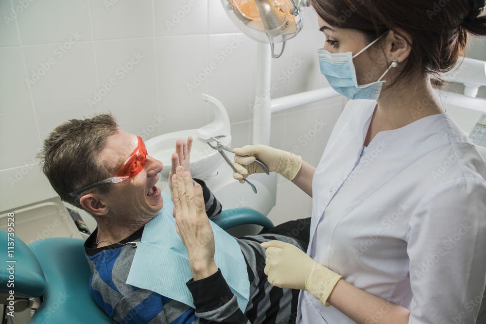 Obraz premium The frightened patient in the dentist's chair. The man is afraid to treat teeth. Dr. dentist .calms the patient