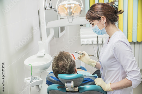 dental care concept stomatology inspection. the patient lies in a chair in dentistry in front of him a hand with drill. the dentist is in the office beside the chair with the patient