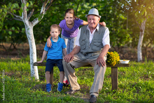Grandfather with grandchildren sitting on a bench in the orchard