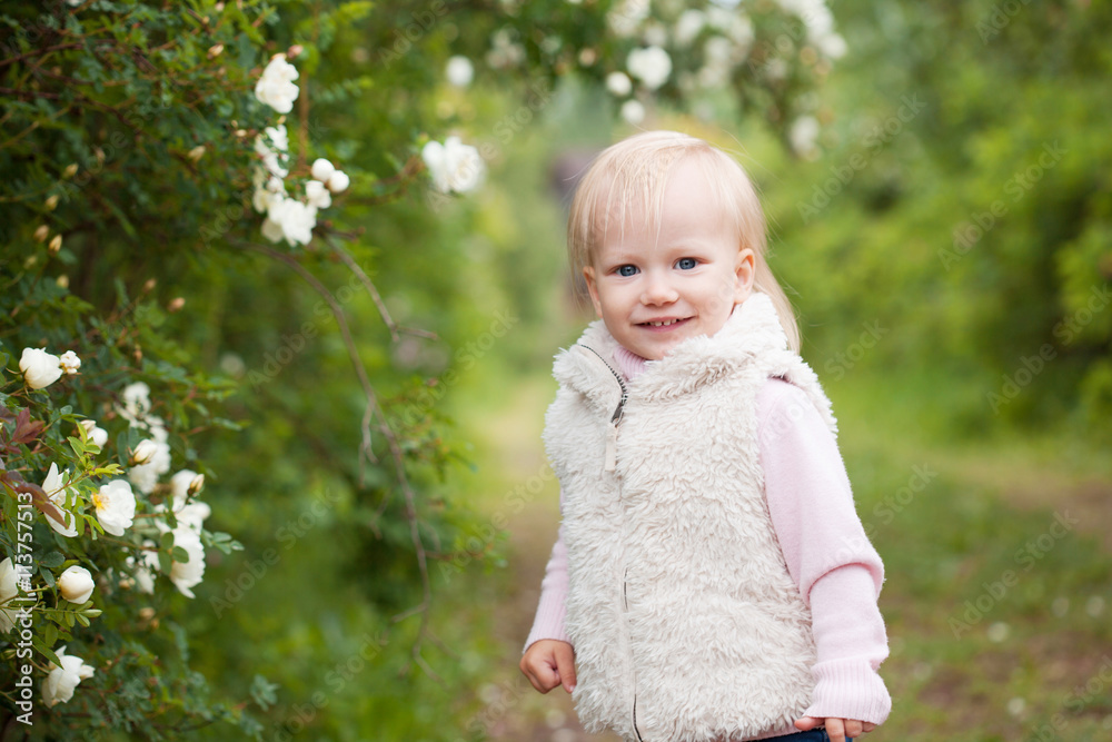 Cute baby girl with blonde hair in the blooming garden