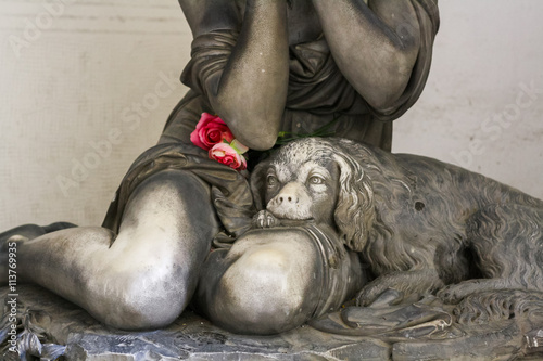 Statue of a dog on knees of grieving girl on monumental cemetery of Staglieno in Genoa.