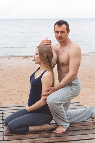 Man and pregnant woman are doing yoga on the beach