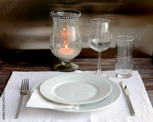 Table setting for dinner. Wooden table with white and transparent  glassware for one person. Burning candle