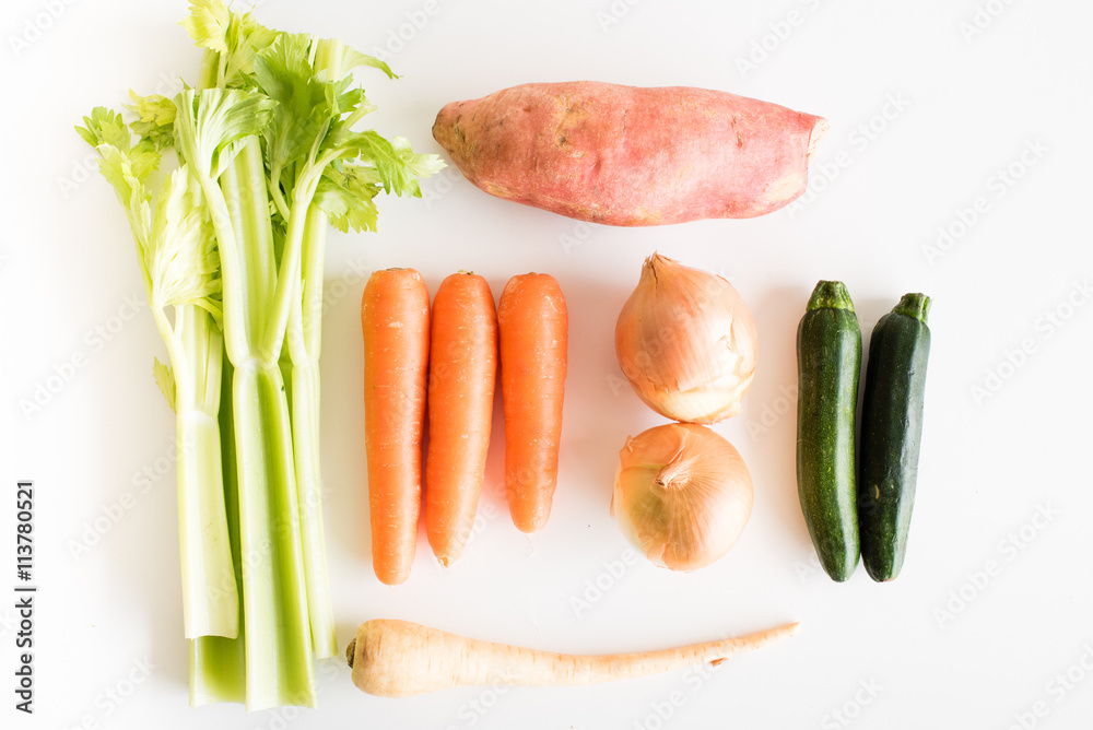 High angle view of celery, carrots, onions, sweet potato, zucchini and parsnip on a white table High angle view of celery, carrots, onions, sweet potato, zucchini and parsnip on a white table