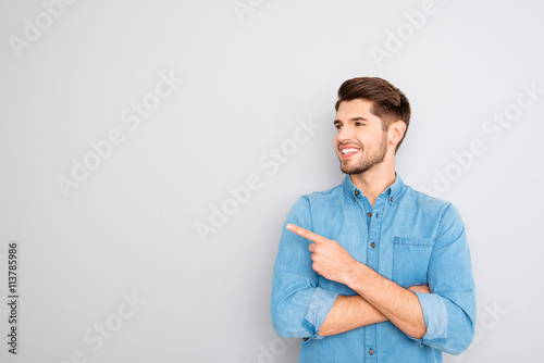 Cheerful young man pointing away on gray background