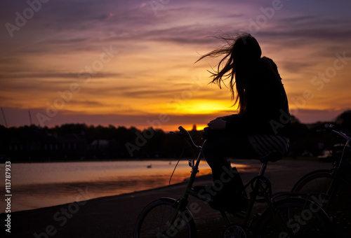 Silhouette of a girl sitting on a bike at sunset