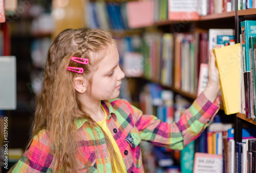 young girl chooses a book in the library