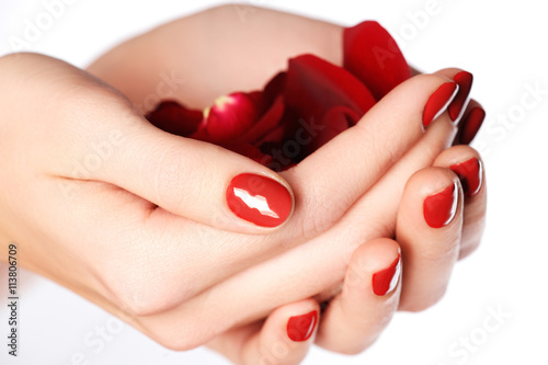 Beautiful female finger nails with red nail close-up on petals. Perfect manicure