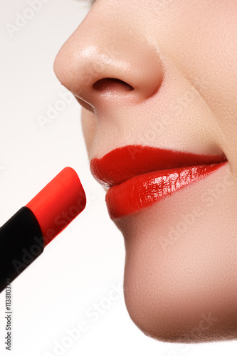 Close-up shot of woman lips with glossy red lipstick. Extreme close-up on model applying red lipstick. Professional make-up
