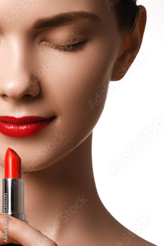 Close-up shot of woman lips with glossy red lipstick. Extreme close-up on model applying red lipstick. Professional make-up