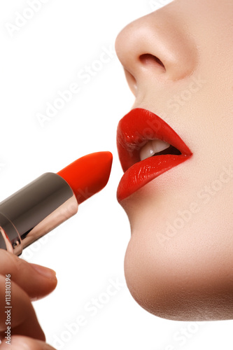 Extreme close-up on model applying red lipstick. Professional make-up