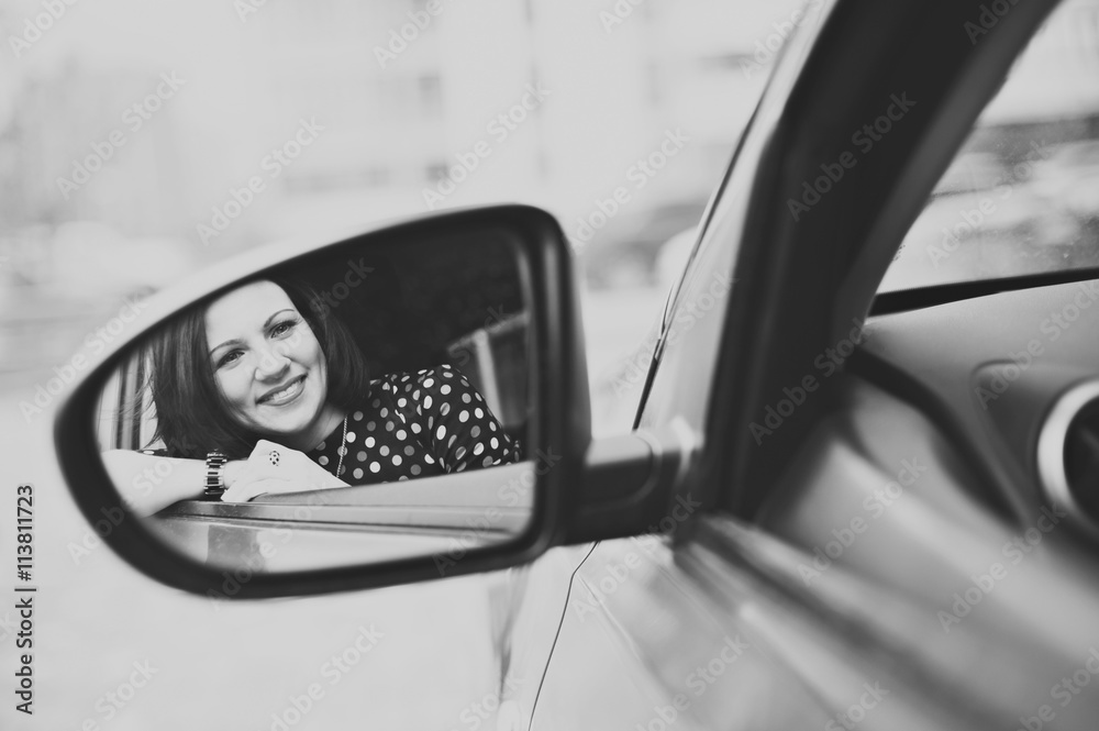 Portrait of young beautiful happy woman in the reflection of the car mirror, close-up, black-and-white image. Portrait of young beautiful happy woman in the reflection of the car mirror, close-up, black-and-white image.