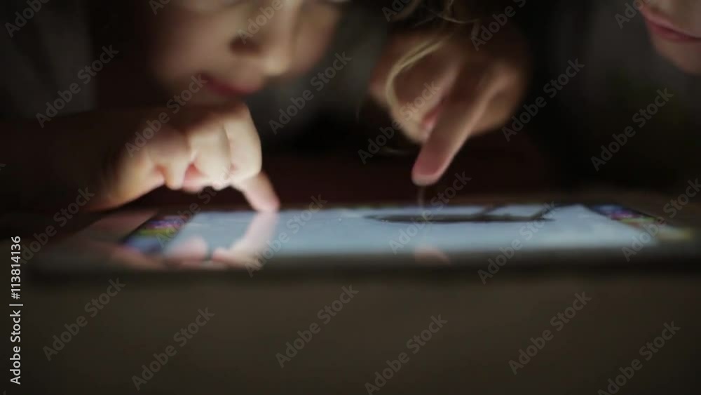 two little girls sisters draw on a tablet PC hiding under a blanket two little girls sisters draw on a tablet PC hiding under a blanket