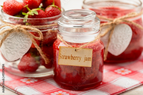 Strawberry jam in glass jars on wooden background.