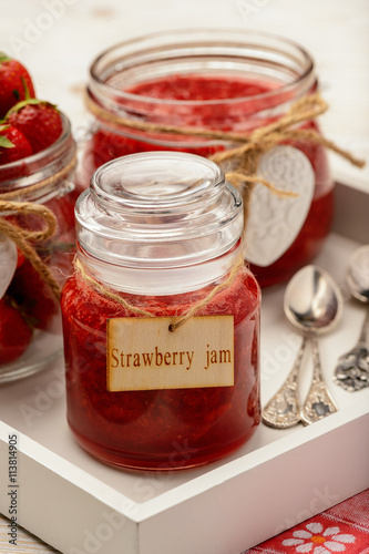 Strawberry jam in glass jars on wooden background.