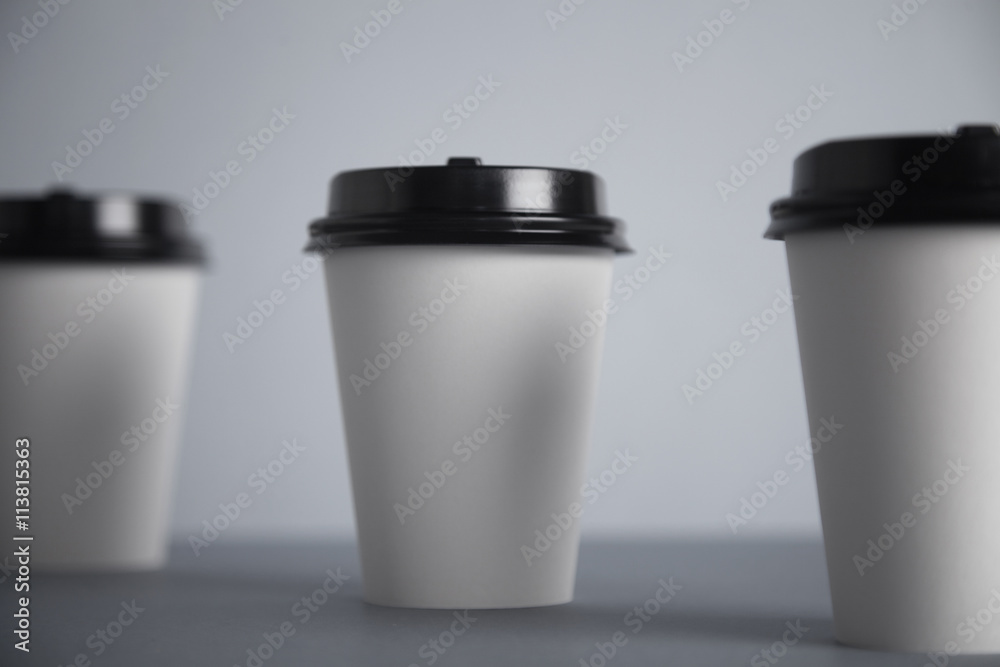 Three take away white paper cups with closed black caps, top view, isolated on simple gray background, focused really close on black cap of central cup Three take away white paper cups with closed black caps, top view, isolated on simple gray background, focused really close on black cap of central cup