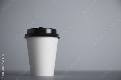 One focused take away white paper cup with black cap presented in front, isolated on side of simple gray background