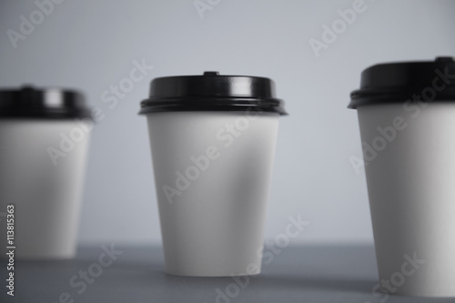 Three take away white paper cups with closed black caps, top view, isolated on simple gray background, focused really close on black cap of central cup