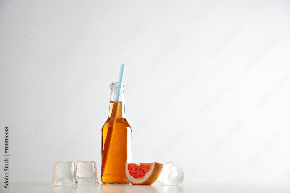 Tasty fresh cider in transparent bottle with blue drinking straw near ice cubes and red grapefruit slice isolated on white Tasty fresh cider in transparent bottle with blue drinking straw near ice cubes and red grapefruit slice isolated on white