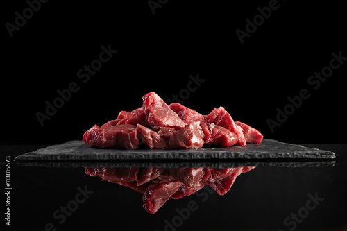 Pieces of raw fresh meat isolated on black on stone board mirrored side view photo