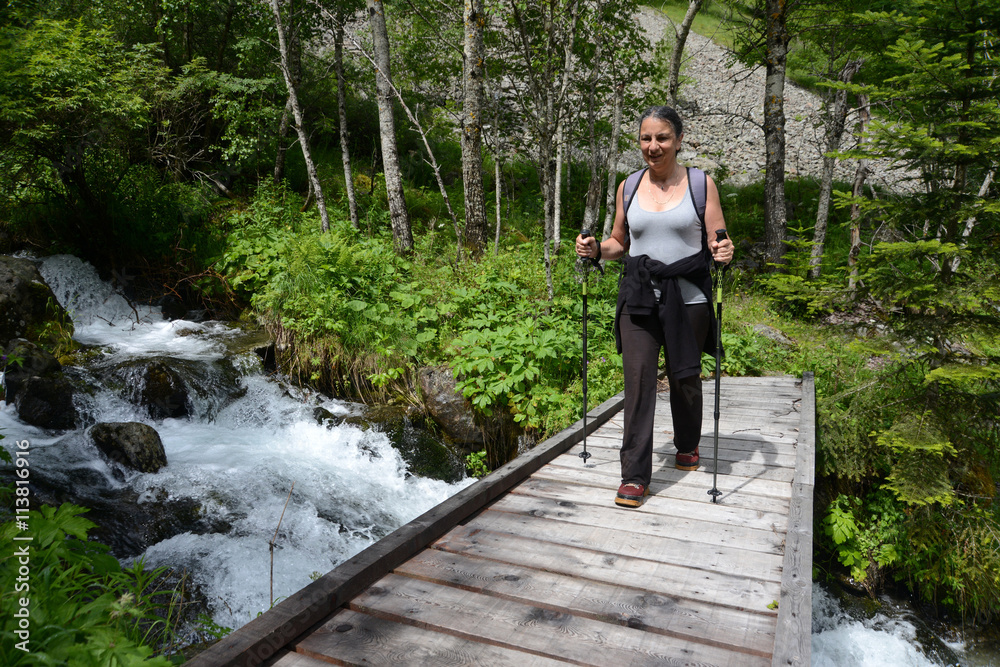 Randonneuse sur un pont traversant la rivière du Prentiq dans le parc national des Écrins Randonneuse sur un pont traversant la rivière du Prentiq dans le parc national des Écrins
