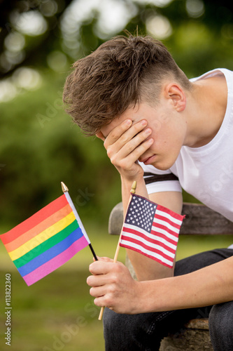 Depressed teenage boy with United States Flag and a Pride flag photo