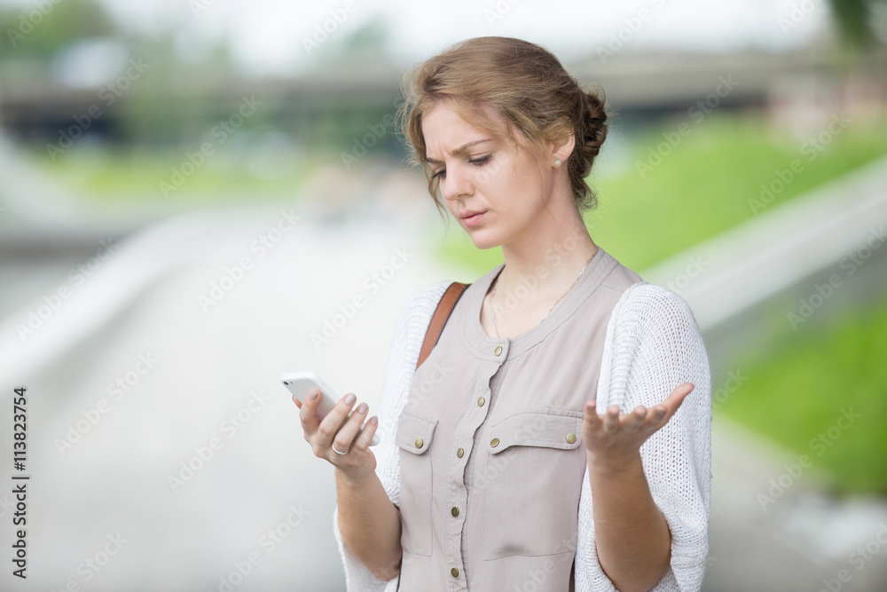 Portrait of stressed beautiful caucasian woman walking on the street and looking at smartphone screen with irritated face expression. Attractive model using mobile phone outdoors in summer Portrait of stressed beautiful caucasian woman walking on the street and looking at smartphone screen with irritated face expression. Attractive model using mobile phone outdoors in summer