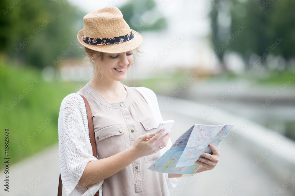 Portrait of happy beautiful casual woman traveler searching direction on map and smartphone. Young traveling female reading map and phone for navigation. Model sightseeing during trip overseas