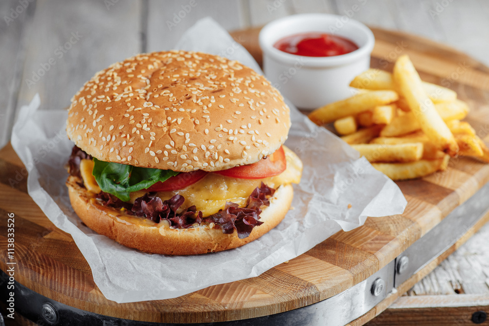 Tasty hamburger and french fries with ketchup on a wooden tray