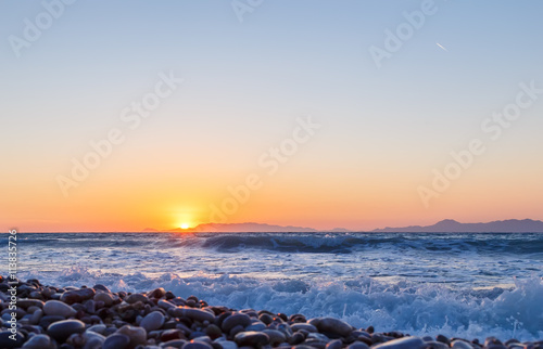 sunset over the islands of Rhodes near the bottom view of a pebble beach © vladimircaribb