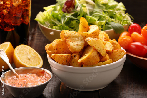 Roasted potatoes with dip and fresh salad on wooden table