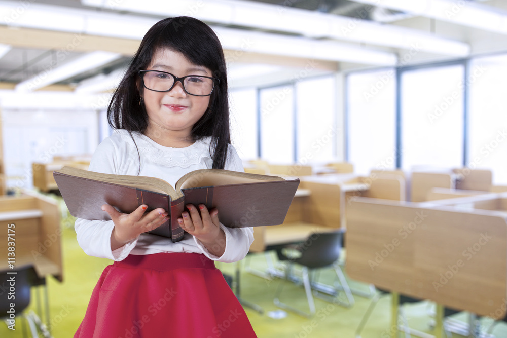 Fototapeta premium Little girl holds book in reading room