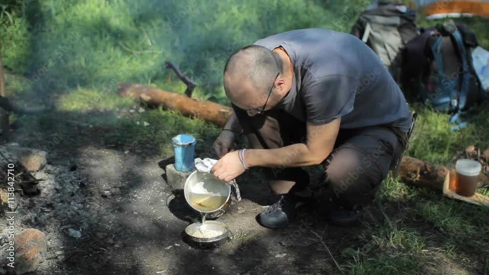 Man prepares porridge in the campaign. Adds the boiling water from the kettle Man prepares porridge in the campaign. Adds the boiling water from the kettle
