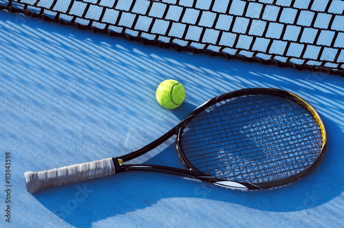 Canvas Print Tennis racket and ball on blue tarmac, net casting shadow