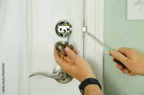 Closeup of a professional locksmith is installing or repairing a new deadbolt lock on a house exterior door with the inside internal parts of the lock visible photo